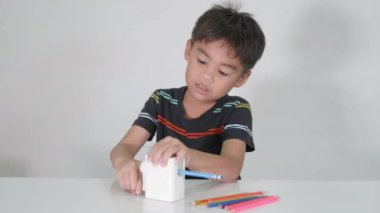 Küçük sevimli çocuk 5-6 yaşlarında. Stüdyo çekimleri sırasında kalem açacağı kullanırken gülümsüyor. Beyaz arka planda izole edilmiş, Asyalı çocuklar okul öncesi renk kalemleri, eğitim konsepti.