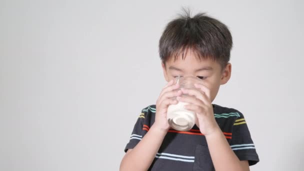 可爱的小男孩 微笑着拿着牛奶杯 他在工作室里喝着白牛奶 被隔离在白色的背景下 在亚洲孩子的学前班里 日常生活保健食品 — 图库视频影像