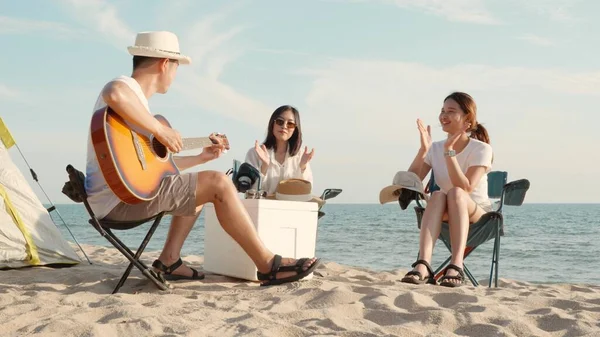 幸せな友人は楽しいギターを演奏し キャンプで拍手をしています彼らはキャンプテントの休暇時間の近くの砂浜で一緒に笑顔日没で 若いアジアのグループの女性と夏の旅行で男屋外 — ストック写真