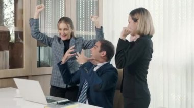 Kazananların başarı projesini kutluyoruz. Üç mutlu iş adamı birlikte iyi haberler aldıkları için heyecanlı. Başarılı projeyi masa başındaki dizüstü bilgisayarla kutluyorlar.