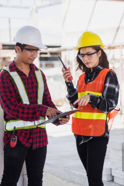 İnşaat alanında konuşan iki Asyalı mühendis mimar erkek ve kadın inşaat işçisi, mühendislik bölümü radyo tartışması yürütme projesi ve inşaat için kontrol çalışanı