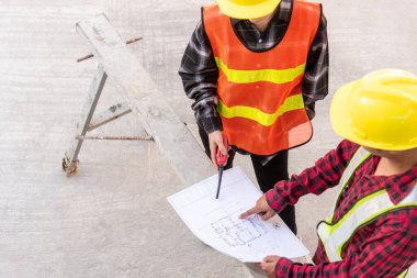Mimar ve müvekkil inşaat alanının zeminindeki binanın planıyla plan oluşturulmasına yardım ediyor. Asyalı mühendis ustabaşı erkek ve kadın işçi toplantı ve planlama inşaat işi, üst görünüm