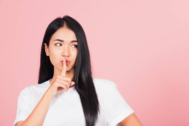Asyalı mutlu bir portre güzel tatlı bir genç kadın gülümsüyor parmaklarını dudaklarına koyuyor sessiz bir jest stüdyosu çekimi pembe arka planda izole edilmiş Taylandlı kadın fotokopi alanından uzaklaşmaya çalışıyor.