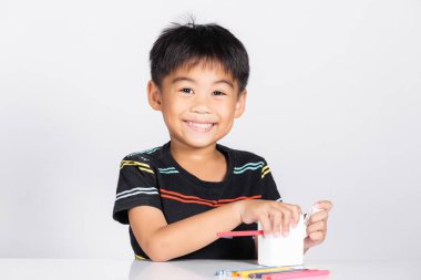 Küçük sevimli çocuk 5-6 yaşlarında. Stüdyo çekimleri sırasında kalem açacağı kullanırken gülümsüyor. Beyaz arka planda izole edilmiş, Asyalı çocuklar okul öncesi renk kalemleri, eğitim konsepti.