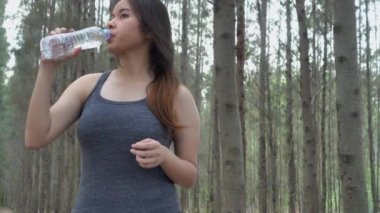 Asyalı güzel koşucu genç bayan sporda müzik dinlerken sabah koşusundan sonra plastik bir şişeden su içiyor, fitness kadını içme suyu içiyor.
