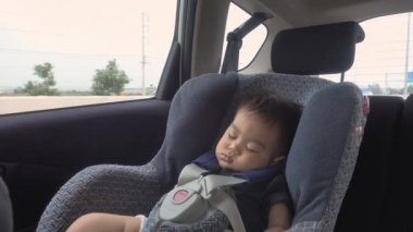 Asya 'lı küçük bebek güvenli çocuk koltuğunda uyuyor. Yolculuk sırasında yolda seyahat ediyor.