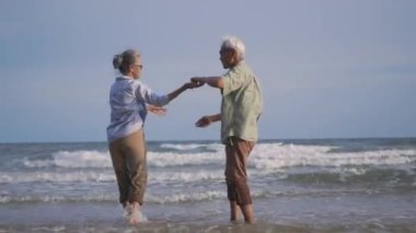 Mutlu Asyalı erkek ve kadın kıdemli çift gülümser dans eder plaj balayında dinlenir aile güneşli bir günde romantik yaşlılar yaz tatilinde seyahat eder emekliler için hayat sigortası yaptırır.