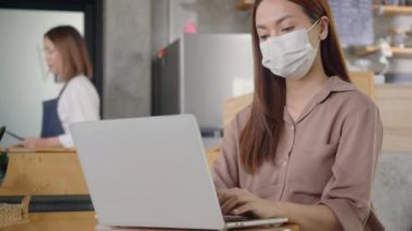 Asyalı genç ve güzel iş kadını kahvede dizüstü bilgisayarını kullanarak gülümsüyor, misafirperver garson müşteriye siparişi seçmesinde yardım ediyor, kafede dizüstü bilgisayarla çalışan bir kadın.