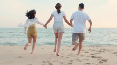 Mutlu arkadaşlar el ele tutuşup hayatın tadını çıkarıyorlar kumsalda birlikte özgürlüğün tadını çıkarıyorlar gün batımında tatil tatilinde genç Asyalı kadın ve erkek yaz seyahatinde, insanların yaşam tarzı