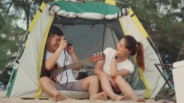 Genç, sevgi dolu bir çift kamp yaparken kamerayla fotoğraf çekiyor. Tatil tatilinde sahilde, gün batımında kamp çadırında oturuyor. Genç Asyalı bir grup kadın ve erkek yaz gezisinde.