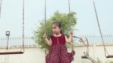 Mutlu gülümseyen küçük kız dışarıda oyun oynarken salıncakta sallanırken eğlen, özgürlük çocuğu yazın günbatımında zincir sallarken.