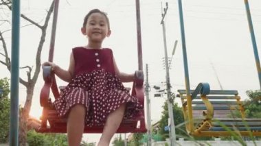 Mutlu gülümseyen küçük kız dışarıda oyun oynarken salıncakta sallanırken eğlen, özgürlük çocuğu yazın günbatımında zincir sallarken.