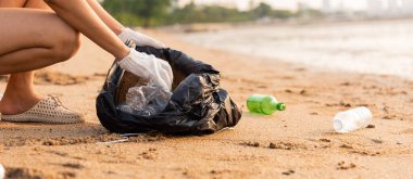 Plajı temizlemek için plastik poşet içine plastik şişe karıştıran gönüllü bir kadın, çöpleri temizleyen bir kadın, ekoloji konsepti ve Dünya Çevre Günü, Dünya 'yı Kurtarma Günü.