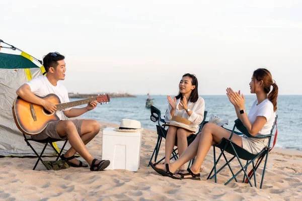 幸せな友人は楽しいギターを演奏し キャンプで拍手をしています彼らはキャンプテントの休暇時間の近くの砂浜で一緒に笑顔日没で 若いアジアのグループの女性と夏の旅行で男屋外 — ストック写真