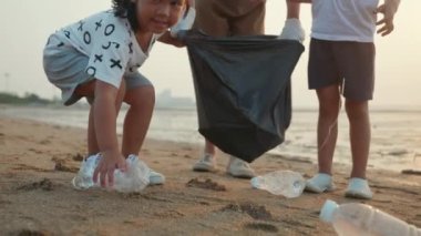Anne ve çocukları gün batımında, ekoloji ve dünya çevresini kurtarmak için çöpleri temizliyor ve plastiği siyah poşetlere dolduruyor.