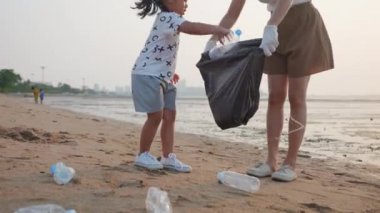 Gönüllü aile, plajı temizlemek için plastik poşet içine plastik şişe karıştırıyor. Anne ve kız gün batımında çöpleri temizliyor. Ekoloji ve Dünya Çevre Günü.
