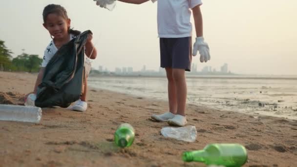 ボランティアの幸せな家族の子供たちは ビーチをきれいにするためのゴミプラスチック製の袋にプラスチックボトルを選ぶ 日没時にゴミをきれいにする子供たち 生態系と世界環境の日 地球の概念を保存 — ストック動画