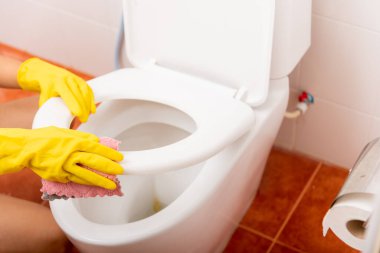 Asyalı bir kadının elleri klozet kapağını pembe bezle temizliyor evdeki tuvaleti siliyor, sarı lastik eldivenler takan bir kadın oturuyor, banyoyu temizliyor ya da yıkıyor, temizlikçi sağlık hizmetleri konsepti.