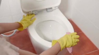 Klozet kapağını pembe bezle temizleyen kadın, sarı lastik eldiven giyen kadın oturup tuvaleti temizliyor, temizlikçi sağlık konsepti.
