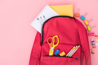 Kırmızı okul çantasının en üst düzlükte yatışı ve çocuk eğitimi için aksesuar araçları pembe arka planda, okula dönüş kavramı ve kullanmak için fotokopi alanı
