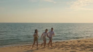 Mutlu arkadaşlar el ele tutuşuyor kumsalda kumsalda eğlenceli bir özgürlüğün tadını çıkarıyorlar gün batımında tatilde deniz kenarında, genç Asyalı grup kadın ve erkek yaz seyahatinde, insanların yaşam tarzında
