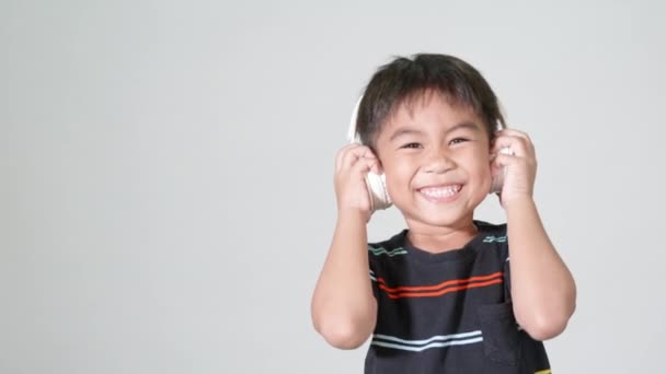 小さなかわいい子供の男の子5 6歳スタジオで無線ヘッドフォンで音楽を聴く白い背景に隔離されたショット 幸せなアジアの子供たちは オーディオとダンスを聞いて笑って エンターテイメントライフスタイル — ストック動画