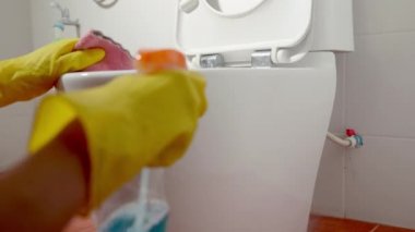 Sıvı sprey ve pembe bez kullanarak klozet kapağını temizleyen kadın evdeki tuvaleti siliyor, sarı lastik eldivenler takan kadın oturuyor ve klozet temizleyici tuvalet temizleyicisi, sağlık hizmetleri konsepti.