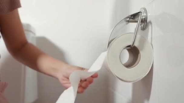 手拉着卫生纸滚筒擦拭 女人坐在马桶上 她拿着并撕破了墙上的白色纸巾在浴室里擦拭 医疗保健理念 — 图库视频影像
