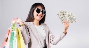 Gözlüklü, kendine güvenen, alışveriş torbaları tutan, elinde para banknotları olan, mutlu Asyalı genç bayan stüdyosu beyaz arka planda izole edilmiş mutlu, mutlu, genç bir bayan.