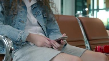 Havaalanı kapısındaki yolcu kadın uçuş için akıllı telefon çalar. Hipster kadın terminal koridorunda oturur ve cep telefonu kullanır.