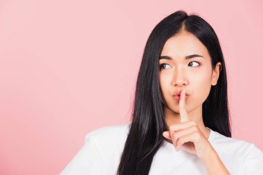 Asyalı mutlu bir portre güzel tatlı bir genç kadın gülümsüyor parmaklarını dudaklarına koyuyor sessiz bir jest stüdyosu çekimi pembe arka planda izole edilmiş Taylandlı kadın fotokopi alanından uzaklaşmaya çalışıyor.