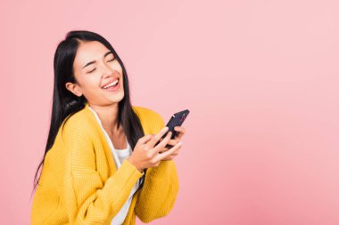 Mutlu bir Asyalı portresi güzel, güzel bir genç kadın elinde cep telefonuyla gülüyor, stüdyo çekimleri pembe arka planda, komik akıllı telefon kullanan bir kadın kazanan hareketi yapıyor.
