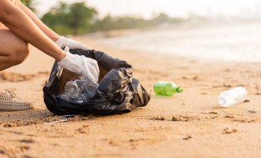 Plajı temizlemek için plastik şişeyi çöp poşetine atan gönüllü bir kadın, gün batımında çöpleri temizleyen bir kadın, ekoloji konsepti ve Dünya Çevre Günü, Dünya 'yı Kurtarma Günü.