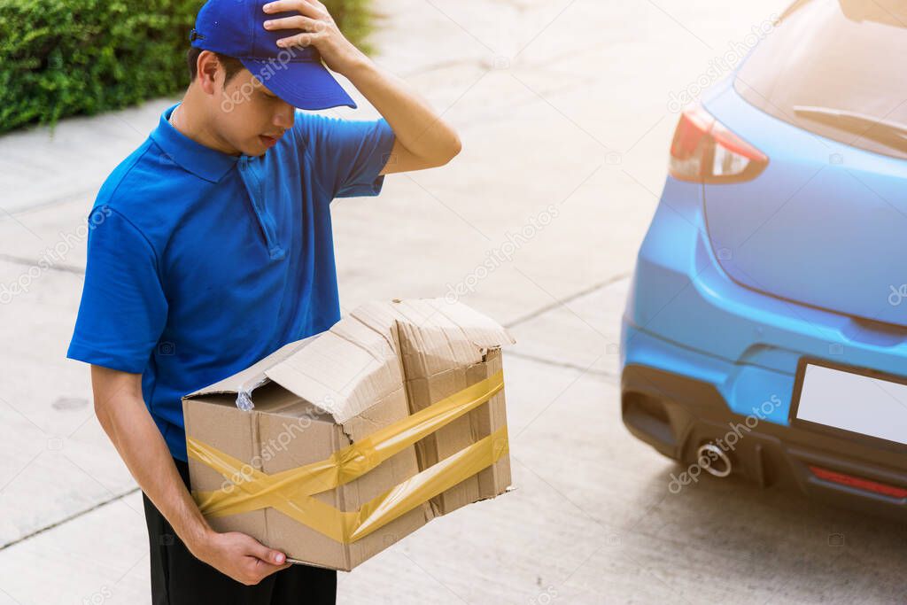 Asian young delivery man in blue uniform he emotional falling courier hold damaged cardboard box is broken at door front home, Accident bad transport shipment or poor quality delivery service concept