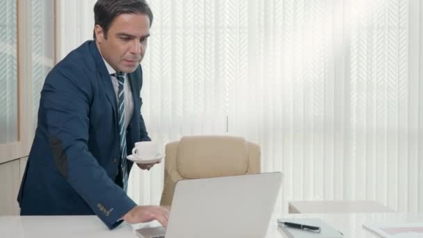 朝のコーヒーカップを飲みながらリラックスしたオフィスの窓辺の仕事机から立ち上がる幸せなビジネスマンは ビジネススーツを着用し 休憩時間を楽しんでいます — ストック動画