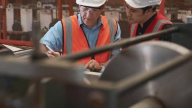 Mühendis çırağına metal levha damgalama makinesi kullanmayı öğretiyor. Endüstriyel ekip tablet bilgisayarlı çeşitli projeler üzerinde çalışıyor. İşçiler fabrikadaki işletim sistemini kontrol etmek için birlikte çalışıyorlar.