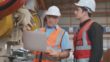 Mühendis çırağına metal levha damgalama makinesi kullanmayı öğretiyor. Endüstriyel ekip dizüstü bilgisayarla çeşitli projeler üzerinde çalışıyor. İşçiler fabrikadaki işletim sistemini kontrol etmek için birlikte çalışıyorlar.