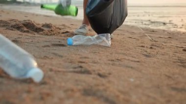 Plajı temizlemek için plastik şişeyi çöp poşetine atan gönüllü bir kadın, gün batımında çöpleri temizleyen bir kadın, ekoloji konsepti ve Dünya Çevre Günü, Dünya 'yı Kurtarma Günü.