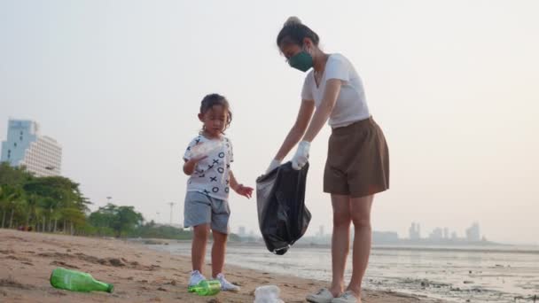 ボランティアの幸せな家族は ビーチ 母と娘をきれいにするために黒のゴミプラスチック製の袋にペットボトルを選ぶ日没 生態系と世界環境の日にゴミをきれいにし 地球の概念を保存 — ストック動画