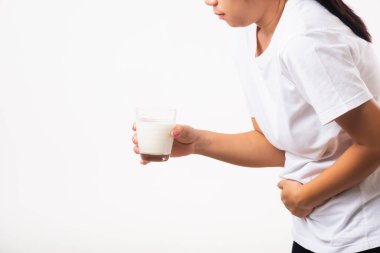 Yakından genç bir kadın hoşgörüsüz, cam sütle el ele tutuşuyor, midesi ağrıyor, laktoza dayanıksızlığı var süt ürünleriyle ilgili sağlıksız bir sorunu var, beyaz arka planda izole edilmiş bir stüdyo çekimi.