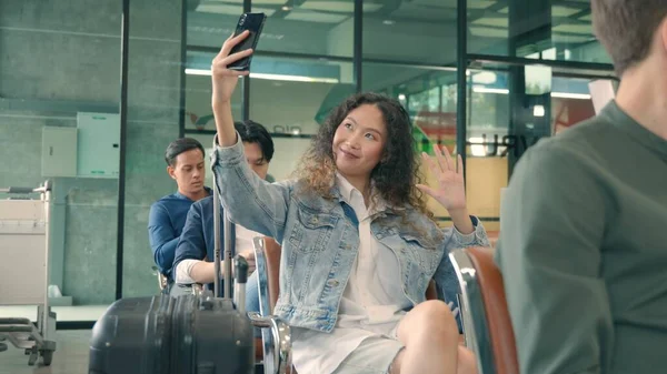 Seyahat tatilinin tadını çıkar. Mutlu Asyalı genç ve güzel kıvırcık saçlı kadın havaalanı terminalinde uçuşunu beklerken akıllı telefonuyla selfie çekiyor. Uluslararası havaalanında turist kız.