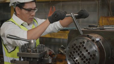 Asyalı profesyonel mekanik operatör üniforma ve gözlük takıyor. Güvenlik görevlileri atölye metal torna fabrikasının, ağır sanayi fabrikasının cıvatalarını sıkıyor.