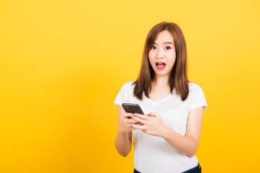 Asyalı mutlu bir portre güzel, gülümseyen bir genç kız tişörtü giyer. Akıllı cep telefonuyla heyecanlanır, telefon izole görünür, stüdyo sarı arka planda fotokopi çekilir.