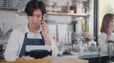Mutlu Asyalı barmen kahve makinası kahve dükkanında telefon alır ve küçük işletme konsepti olan kafede bilgisayardan sipariş alır.