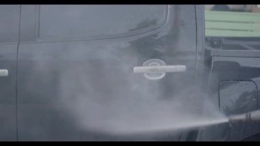 Çamaşır yıkama sırasında su jetinin altında yüksek basınçla araba yıkama, sprey tabanca, genç adam su jeti ile arabayı temizleme ve yıkama