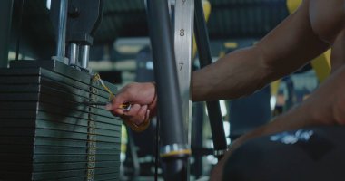 Yakından sporcunun elleri spor aletlerinin ağırlığını egzersiz makinesinde seçer, kas sporcusu spor salonundaki antrenmanı kaldırmak için farklı halter seçeneklerini seçer.