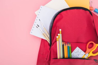 Kırmızı okul çantasının en üst düzlükte yatışı ve çocuk eğitimi için aksesuar araçları pembe arka planda, okula dönüş kavramı ve kullanmak için fotokopi alanı