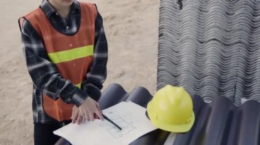 Mimar ve müvekkil inşaat alanının zeminindeki binanın planıyla ilgili yardım planlarını tartıştılar. Asyalı mühendis ustabaşı kadın işçi toplantısı kağıt çizimi projesi hakkında konuşuyor.