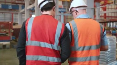 Arka plan görüntüsü. İki işçi koruyucu iş kıyafetleriyle metal yaprak fabrikasına girerken tartışıyor, endüstri imalat makinesi operatörleri yana bakıyor.