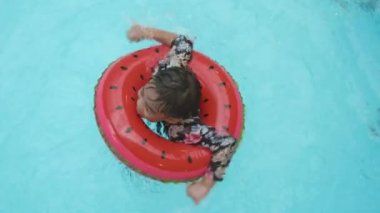 Summer child boy relax at aquapark. Happy Asian kid boy in rubber ring bathes swimming on pool blue water having fun in resort, Summertime vacation concept, top view